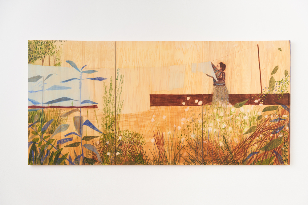 A large painting made of three panels depictures a lush natural scene with shaggy grasses and plants rising from the foreground. Across a yellow, grassy stretch, a woman in profile wearing a bright shirt is see hanging laundry on a line.