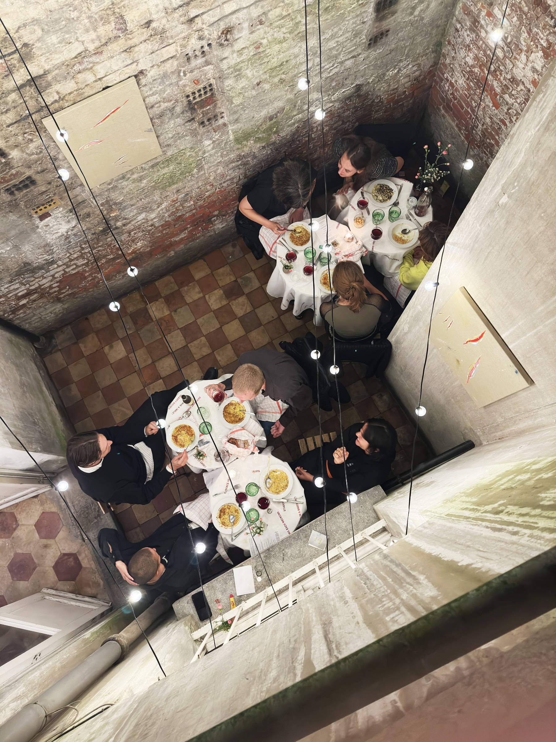 An image from above shows a narrow garden below paved with tiles and four circular dinner tables surrounded by seated guests.