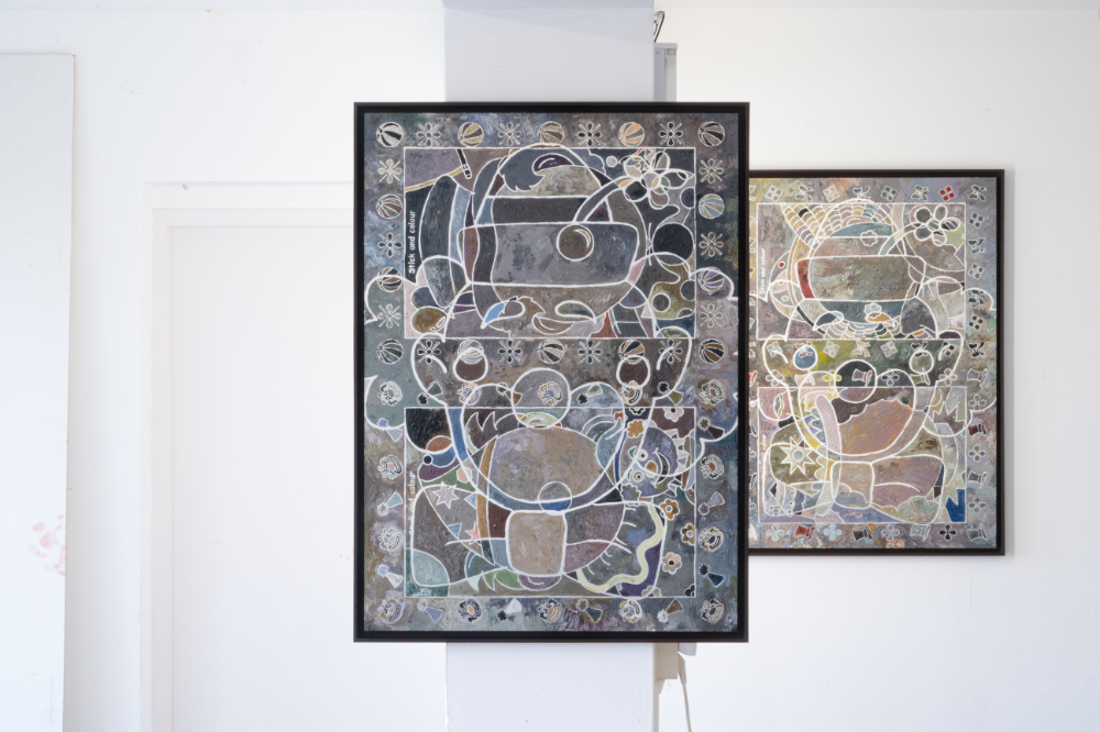 A white gallery show two framed paintings, one in the foreground and one in the background.  The paintings depict the outline of clowns, which are filled in with diffeerent colors and shapes.