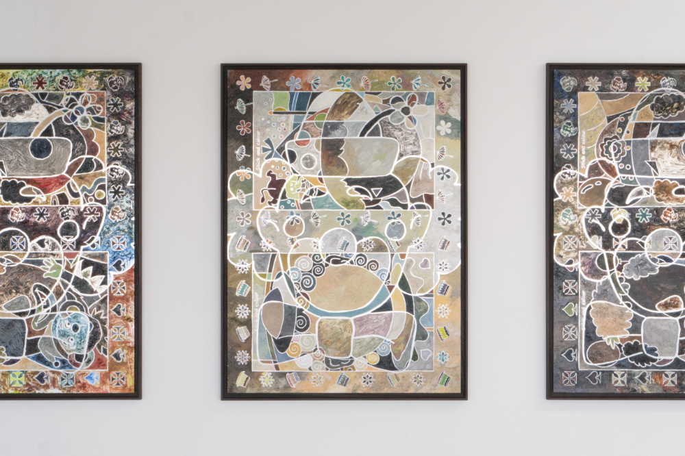 A white wall featuring three framed paintings on a mirrored surface. The paintings depict the outline of clowns, which are filled in with diffeerent colors and shapes.